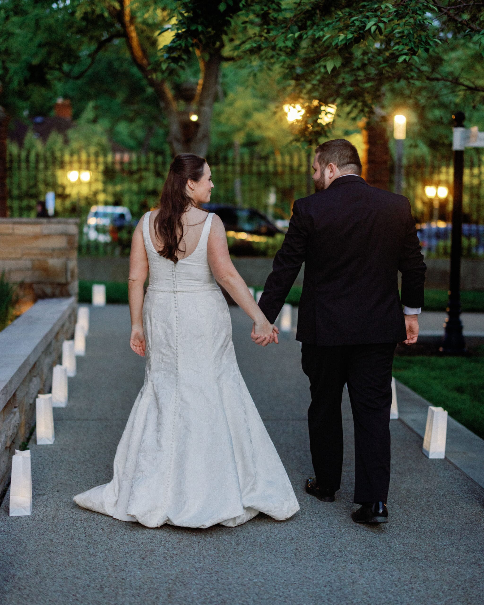 Bride and groom walking hand in hand at outdoor Pittsburgh wedding reception at dusk with soft lighting