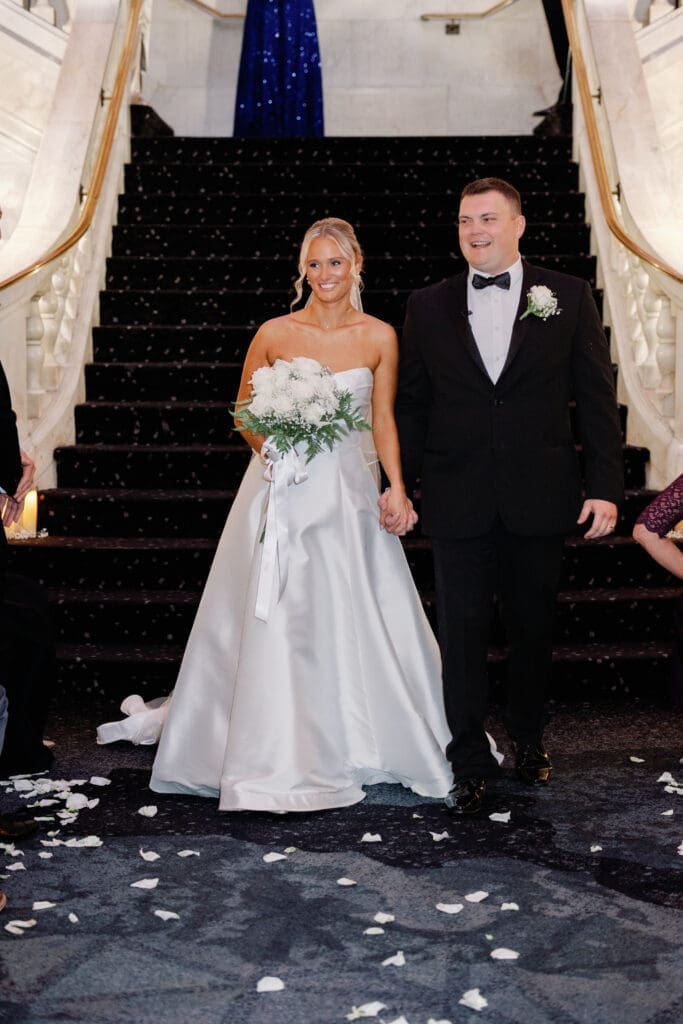 Bride and groom smiling at base of grand staircase after ceremony at Renaissance Hotel Pittsburgh
