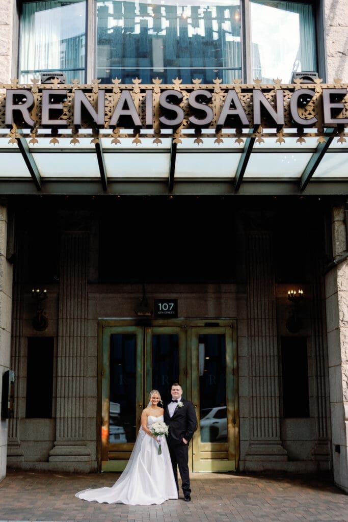 Bride and groom standing under Renaissance Hotel entrance sign in downtown Pittsburgh