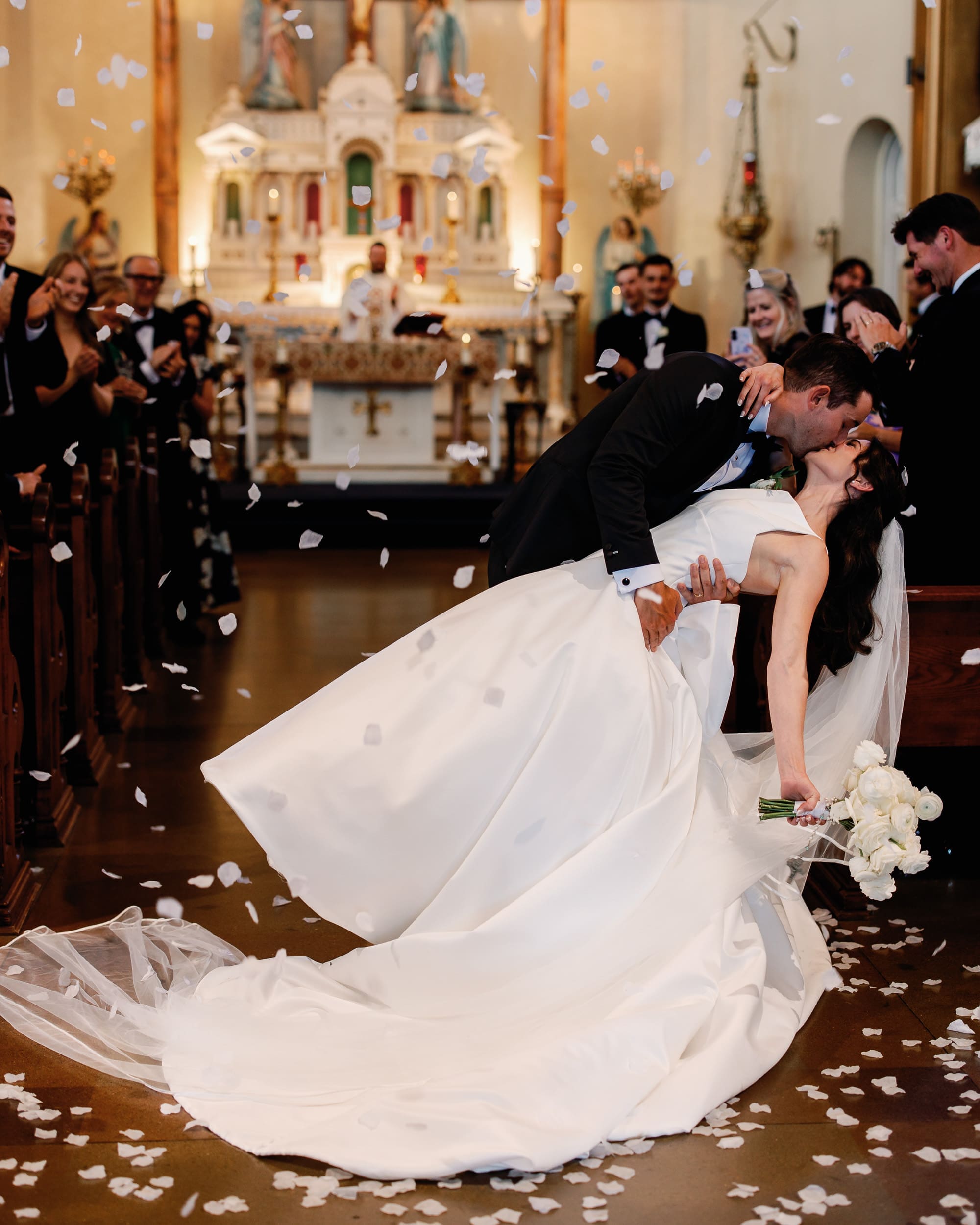 Bride and groom share a celebratory kiss as guests toss flower petals during their wedding ceremony at Pittsburgh Field Club.